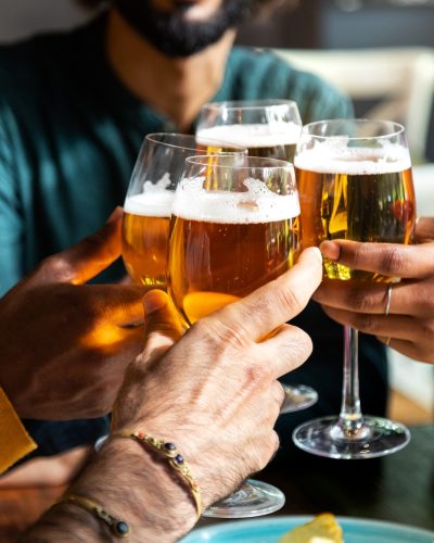 Close up of friends toasting with beer indoors. Friends having fun at bar cheering with beer.
